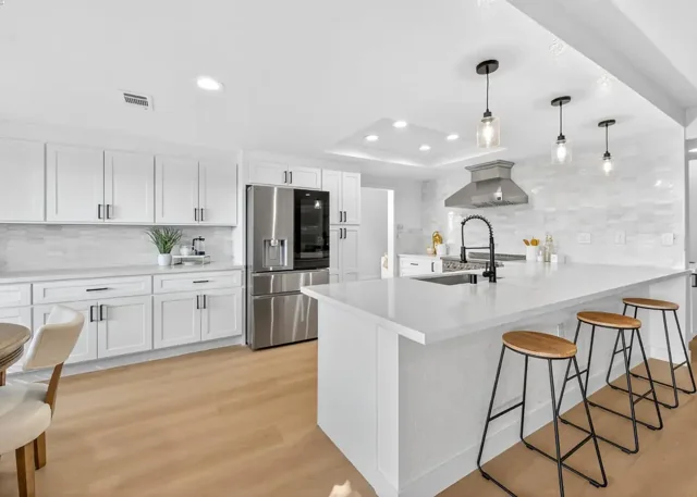 Bright white kitchen remodeled by The House Doctor with a large island and pendant lighting