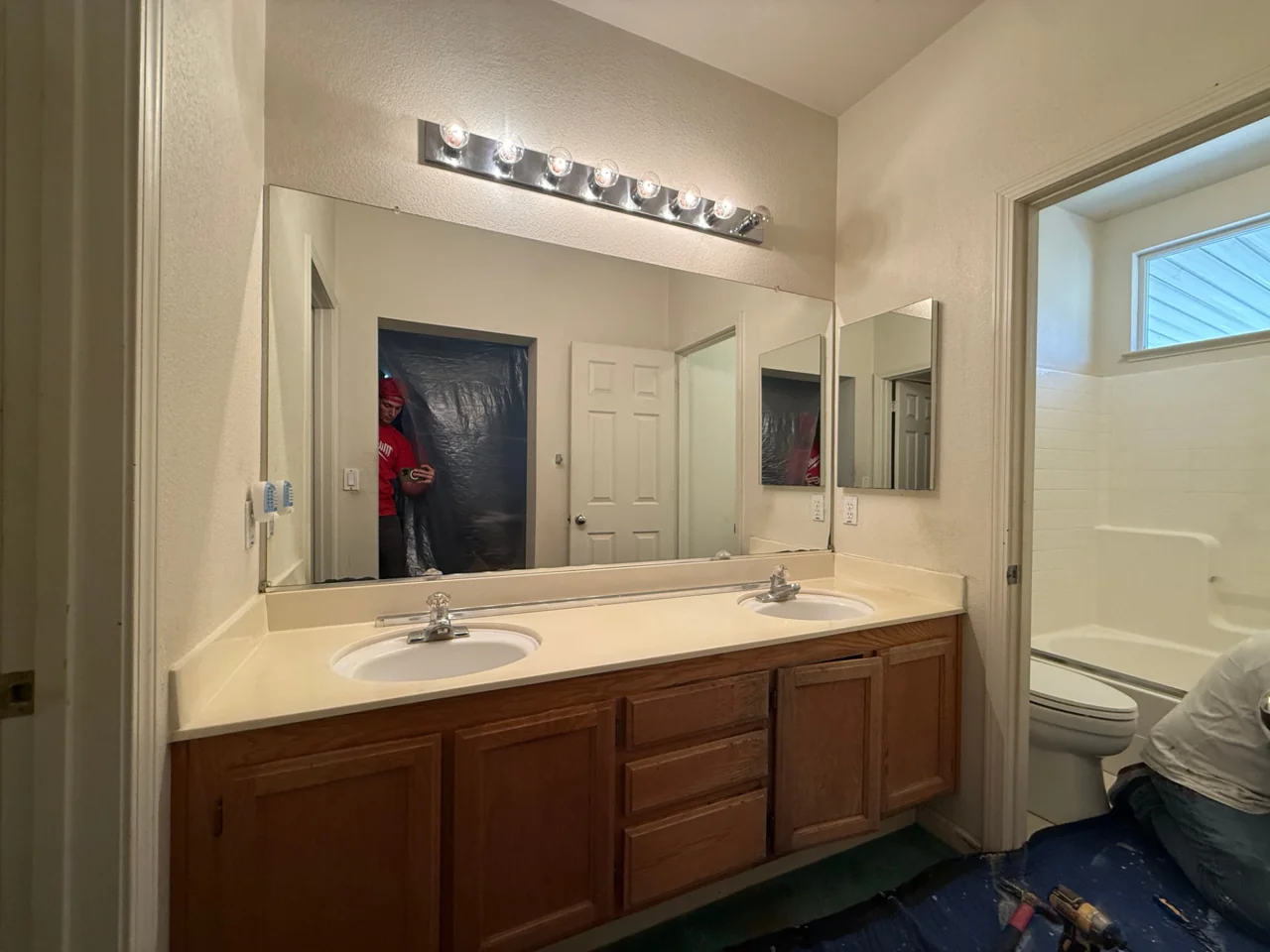 Bathroom before remodeling with oak double vanity, plate mirror and hollywood light bar