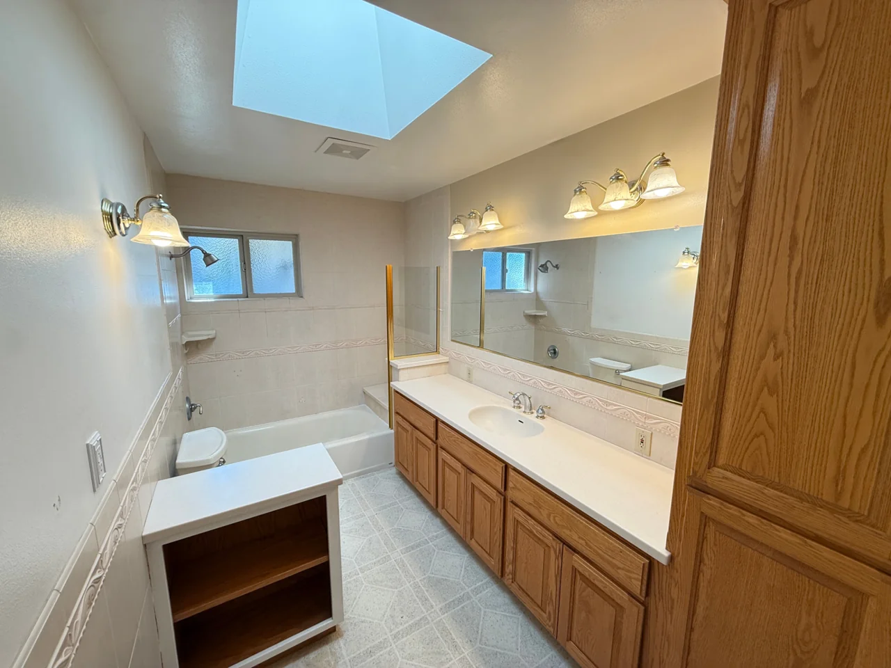 Bathroom before remodeling with oak vanity and bathtub beneath a skylight