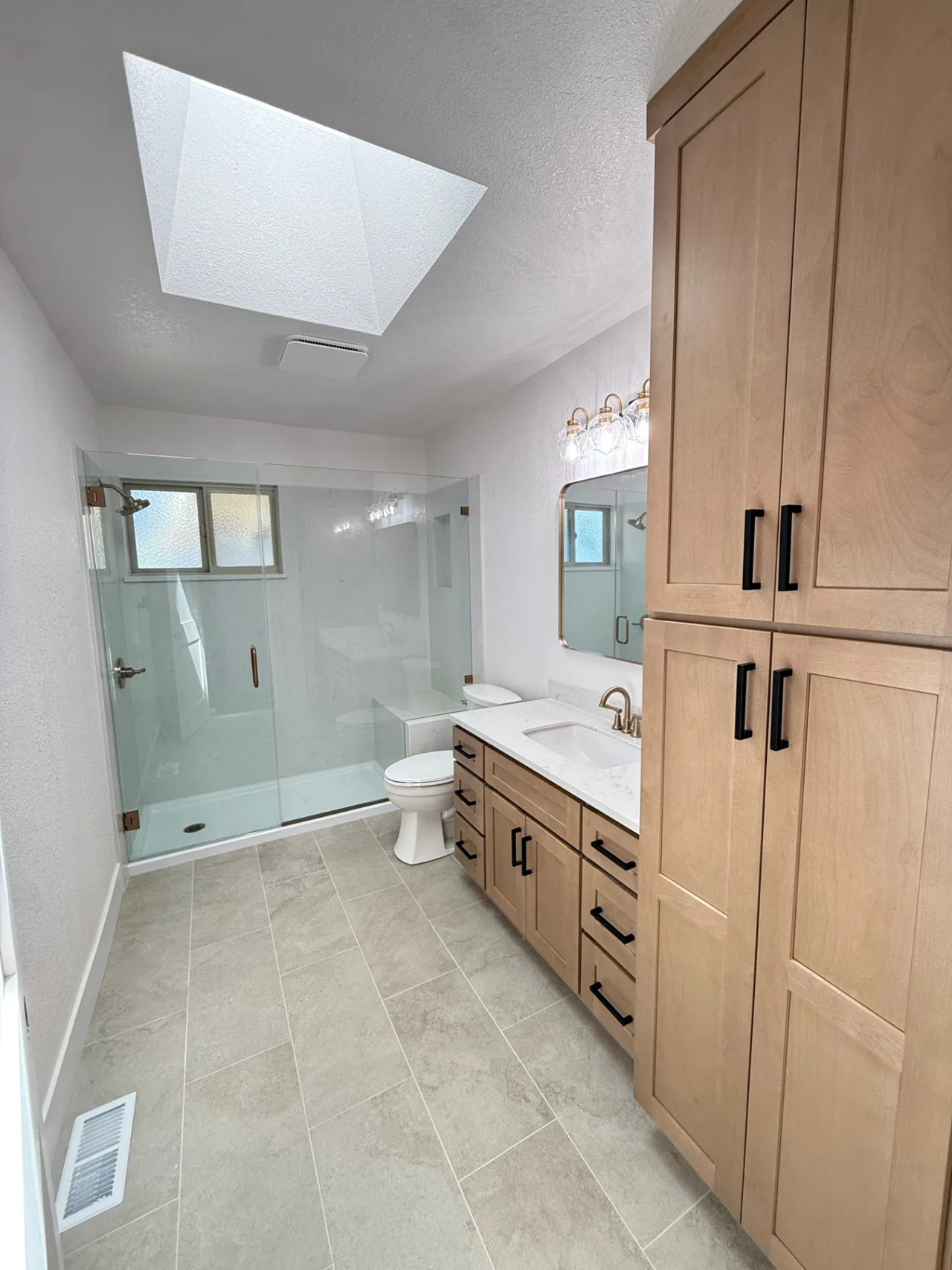 Finished House Doctor bathroom remodel with glass shower and wood cabinets