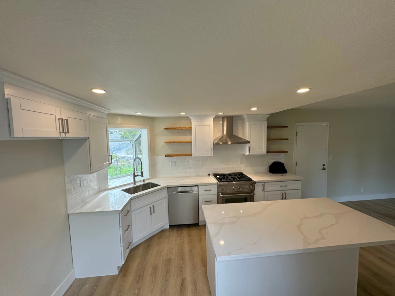 Kitchen after remodeling with white cabinets, floating shelves and quartz island beside the same corner window