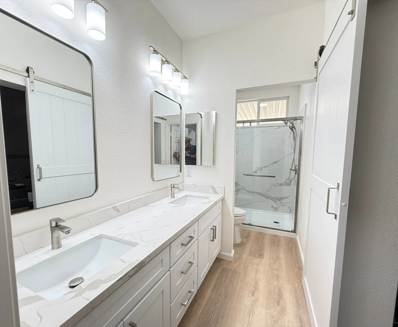 Bathroom after remodeling with white double vanity, marble counters and glass shower