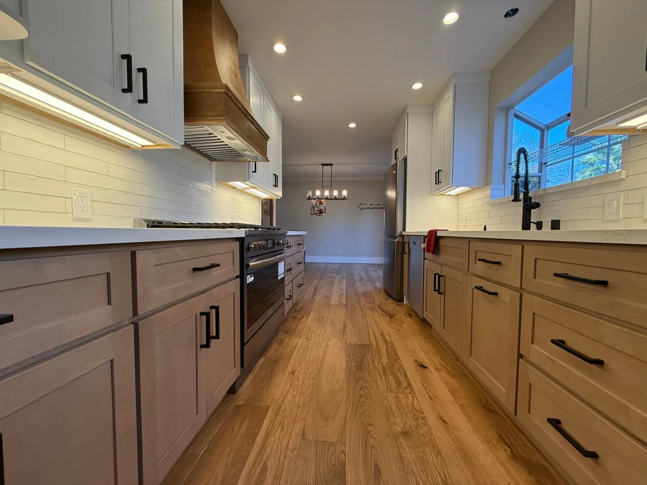 Galley kitchen after remodeling with two-tone cabinets and wood range hood